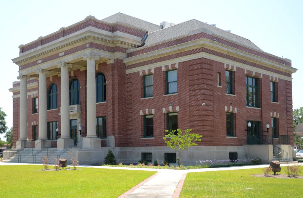 A fine example of a neo-classical red brick and concrete building constructed and used as the county courthouse There are neat lawns and pedestrian access in the foreground