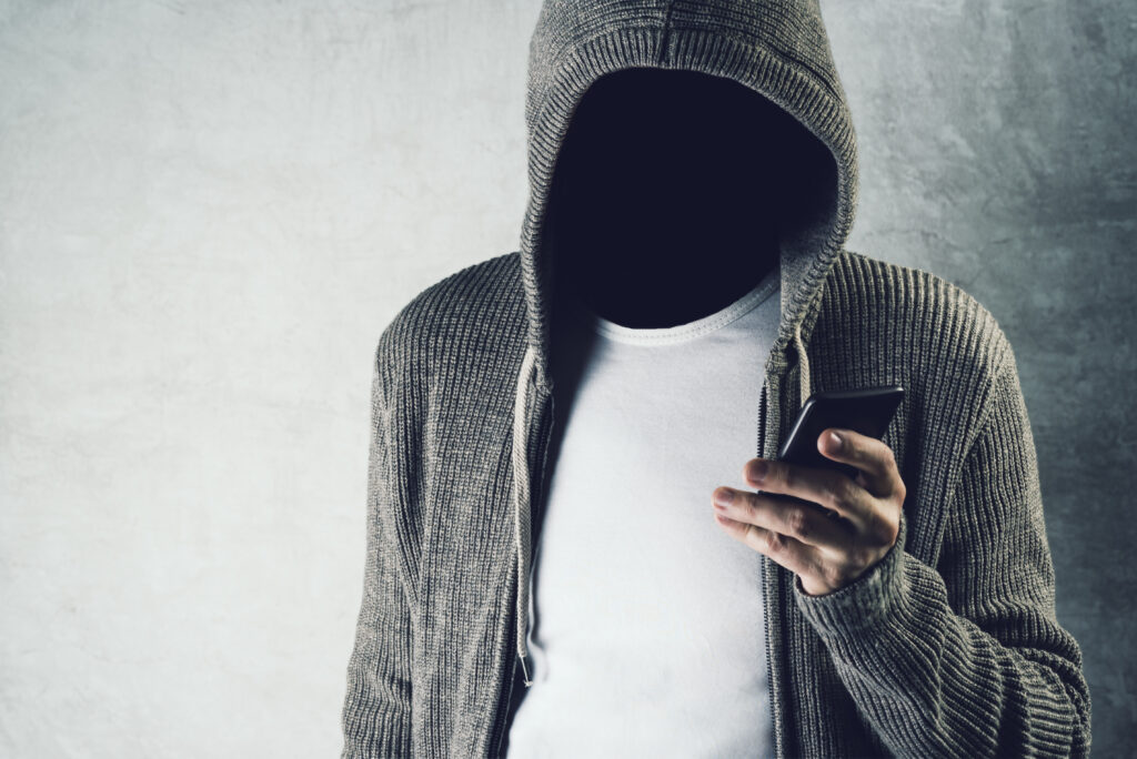 Faceless hooded person using mobile phone identity theft concept during tenant application fraud