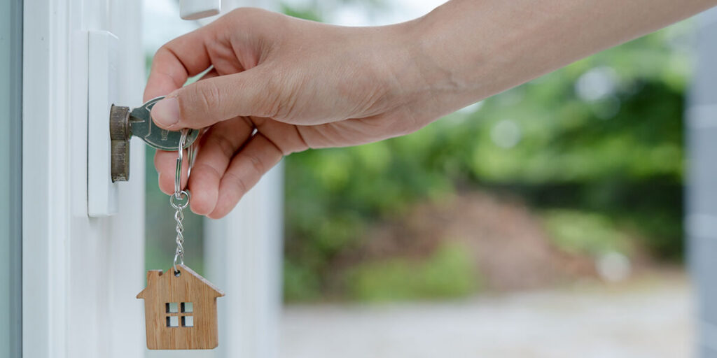 A hand unlocks a residential door with a key, representing tenant and landlord lock-related responsibilities.