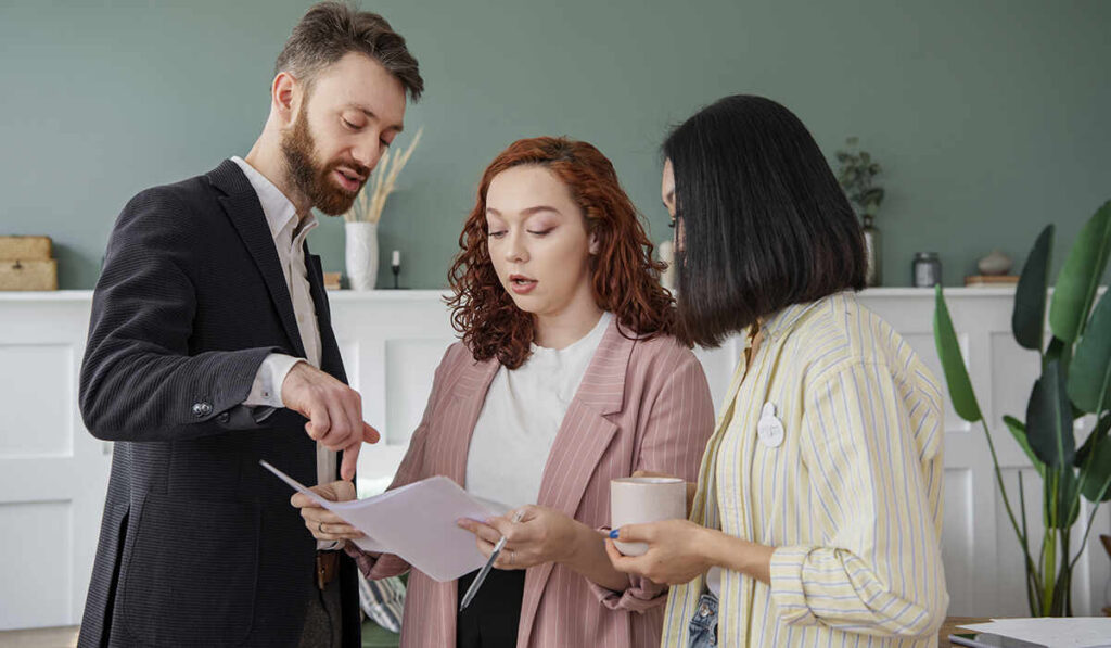 A landlord pointing out lease terms on paperwork while reviewing documents with two tenants.
